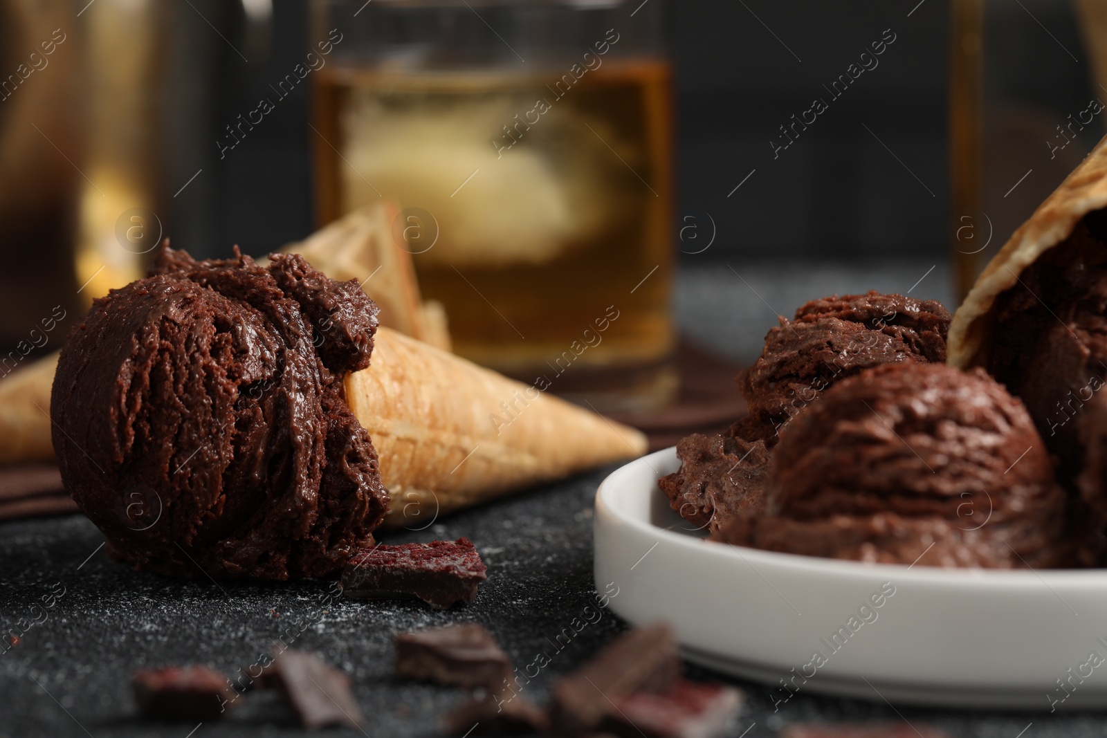 Photo of Tasty ice cream scoops, chocolate crumbs and waffle cones on dark textured table, closeup