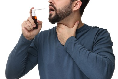 Young man using throat spray on white background, closeup