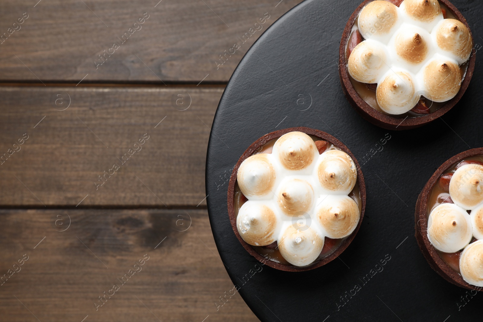 Photo of Delicious salted caramel chocolate tarts with meringue on wooden table, top view. Space for text