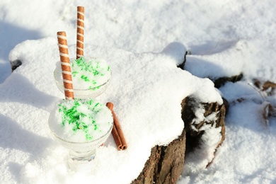 Photo of Glass bowls with tasty ice cream and waffle rolls on snow