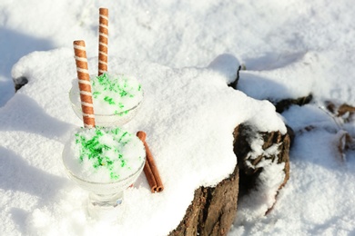 Glass bowls with tasty ice cream and waffle rolls on snow