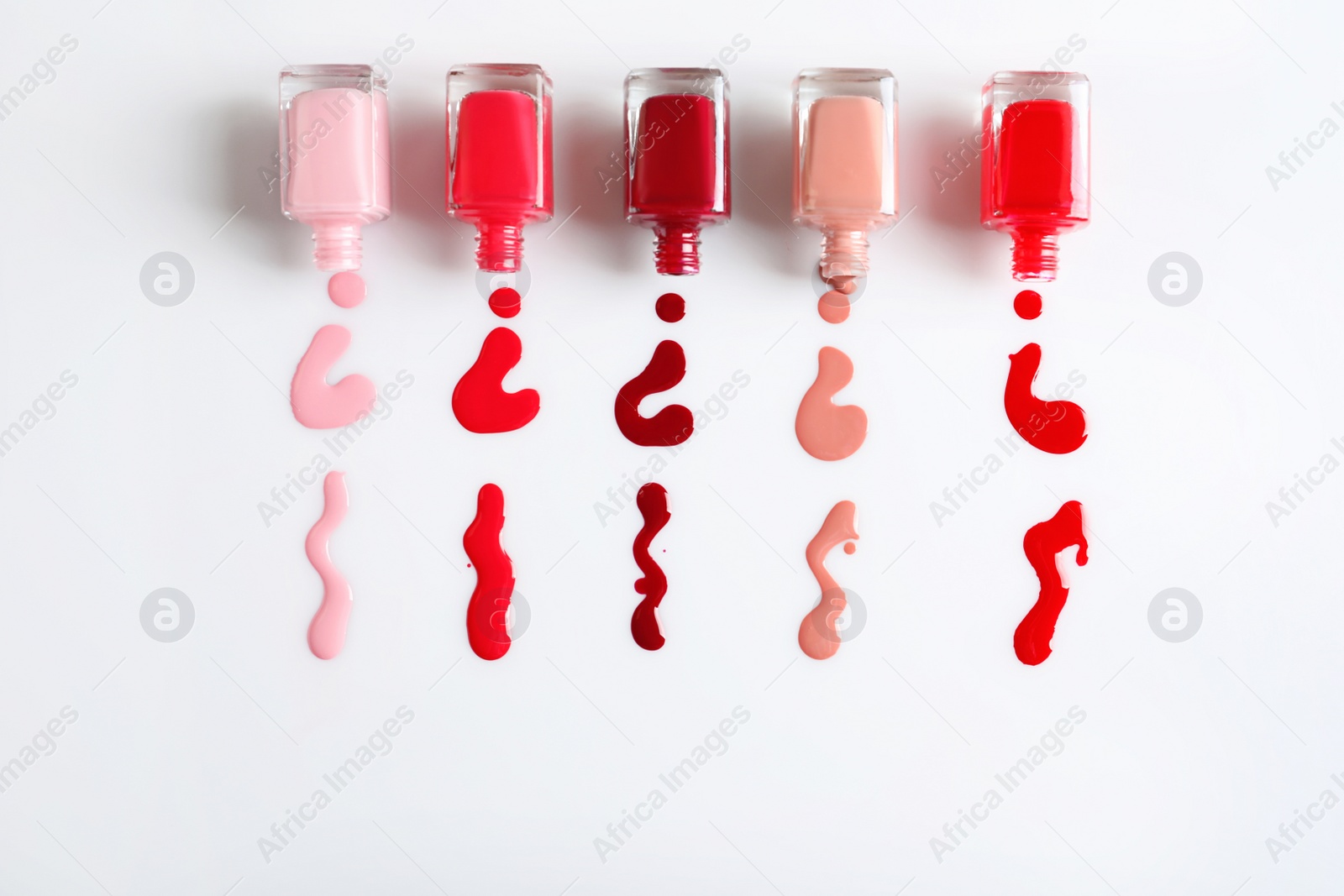 Photo of Spilled colorful nail polishes and bottles on white background, top view