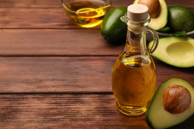 Photo of Glass bottlecooking oil and fresh avocados on wooden table, closeup. Space for text