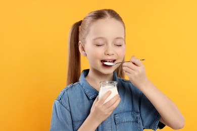 Photo of Cute little girl enjoying tasty yogurt on orange background