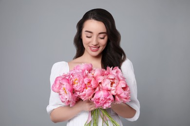 Photo of Beautiful young woman with bouquet of pink peonies on grey background