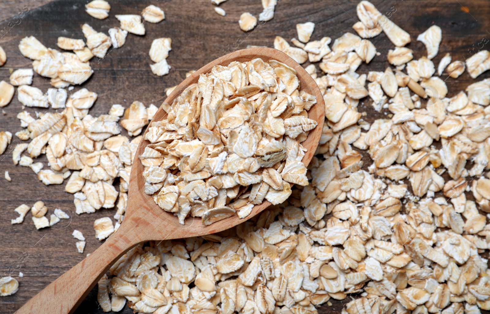 Photo of Spoon with oatmeal on wooden table, flat lay