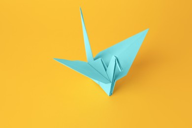 Photo of Origami art. Beautiful light blue paper crane on orange background