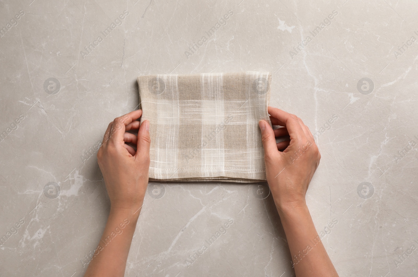 Photo of Woman with checkered kitchen towel on marble background, top view