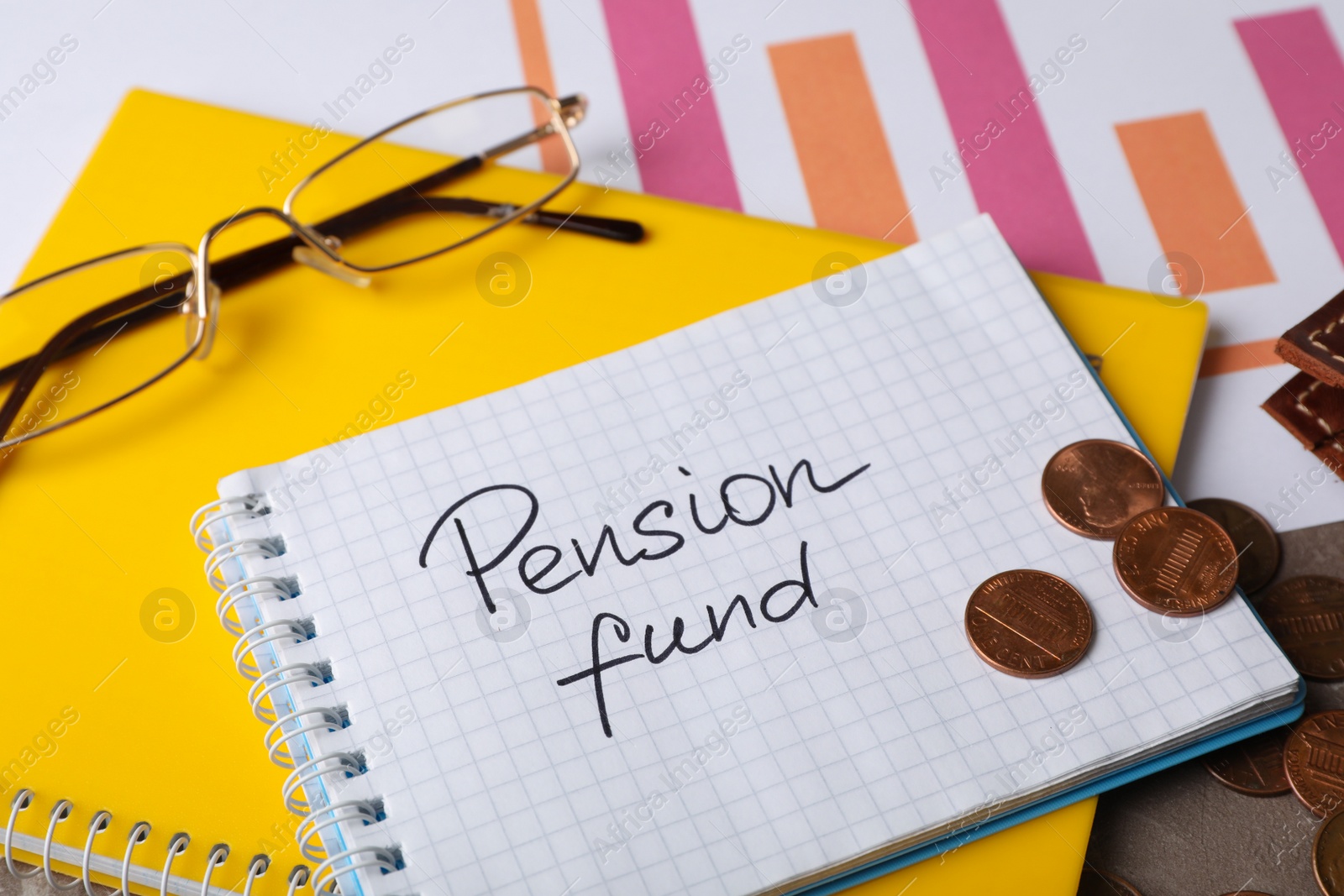 Photo of Coins, glasses and notebook with words PENSION FUND on table