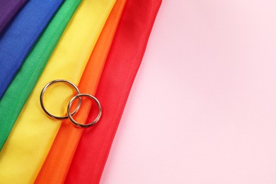 Photo of Rainbow LGBT flag and wedding rings on pink background, top view. Space for text