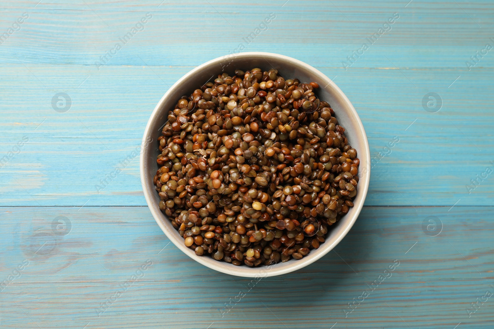 Photo of Delicious lentils in bowl on light blue wooden table, top view