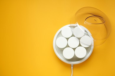 Modern yogurt maker with jars on orange background, top view. Space for text