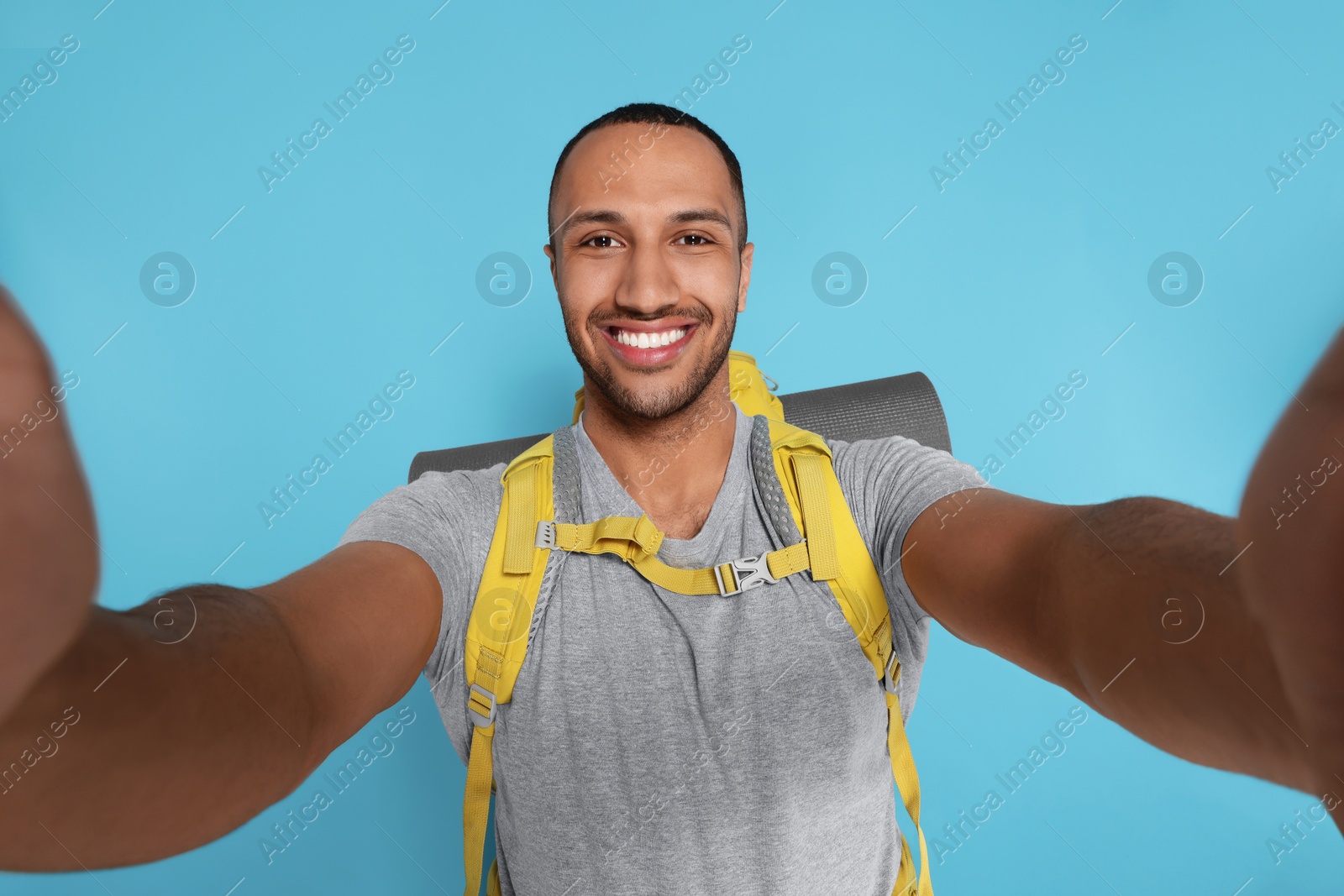 Photo of Happy tourist with backpack taking selfie on light blue background