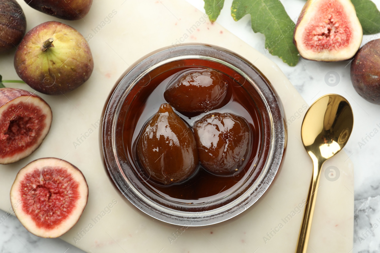 Photo of Jar of tasty sweet jam and fresh figs on white marble table, flat lay