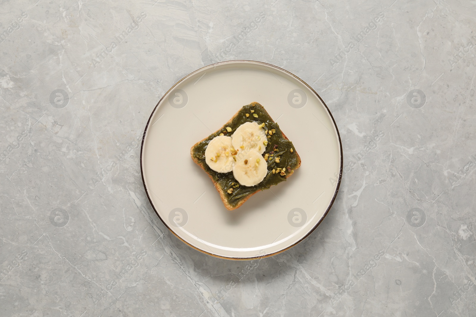 Photo of Toast with tasty pistachio butter, banana slices and nuts on grey marble table, top view