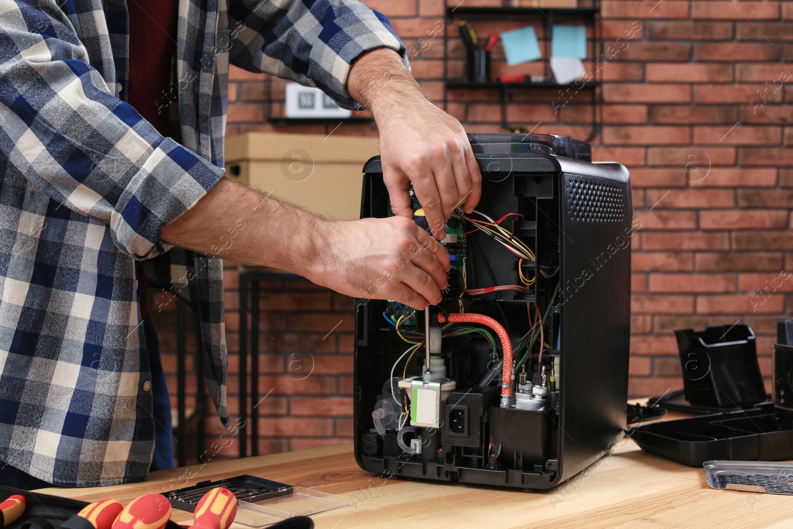 Photo of Man with screwdriver fixing coffee machine at table indoors, closeup