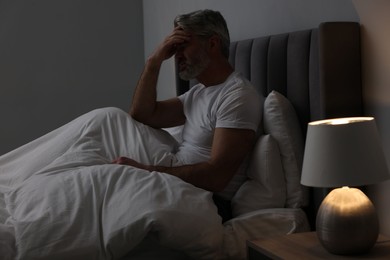 Photo of Mature man suffering from headache in bed at night