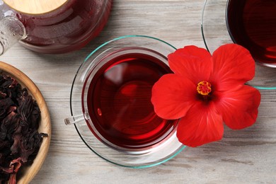 Delicious hibiscus tea and beautiful flower on light wooden table, flat lay