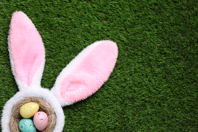 Photo of Headband with bunny ears, painted eggs and space for text on grass, flat lay. Easter holiday