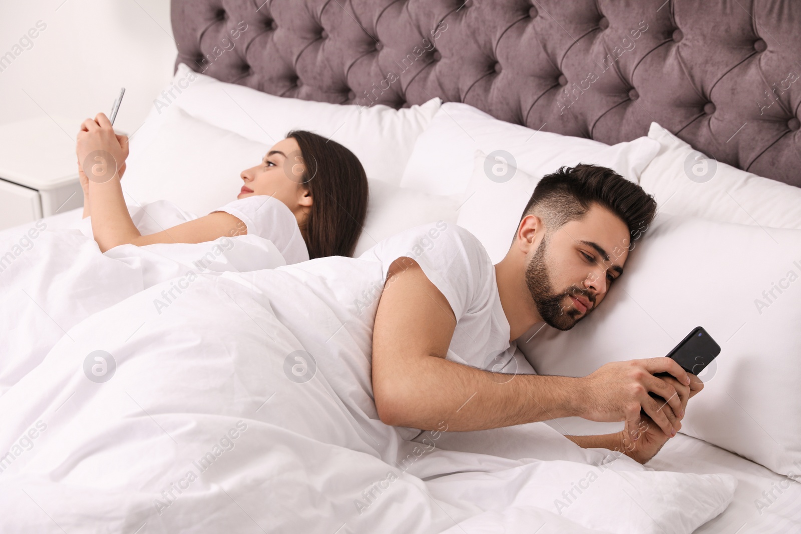 Photo of Young couple addicted to smartphones in bed at home
