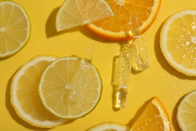 Photo of Skincare ampoules with vitamin C and citrus slices on yellow background, flat lay