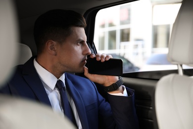 Handsome man with smartphone on backseat of modern car