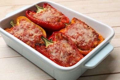 Photo of Tasty stuffed peppers in dish on light wooden table, closeup