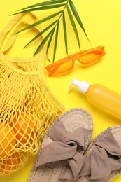 String bag with oranges, sunglasses, cosmetic product, slippers and palm leaf on yellow background, flat lay