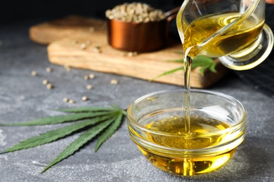 Hemp oil pouring from sauce boat into bowl on grey table