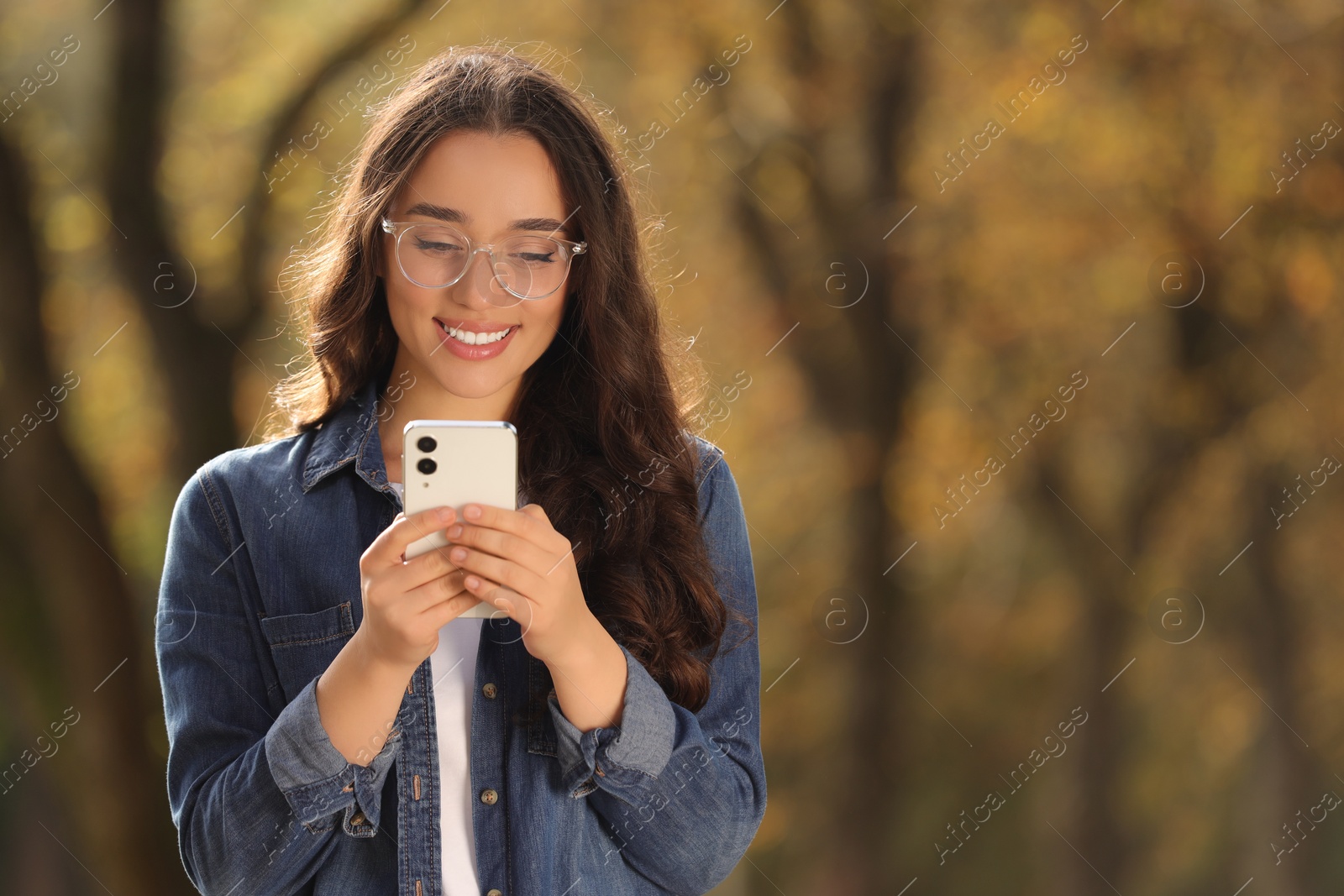 Photo of Young woman using smartphone in autumn park, space for text