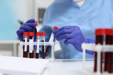 Photo of Laboratory testing. Doctor with blood samples in tubes at white table indoors, closeup