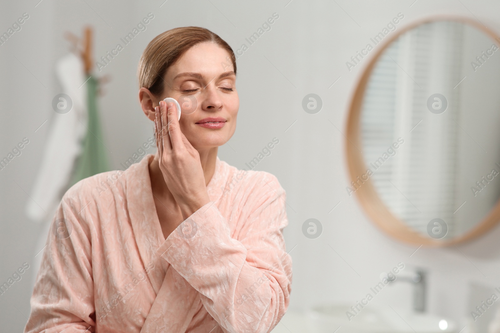 Photo of Beautiful woman removing makeup with cotton pad indoors, space for text