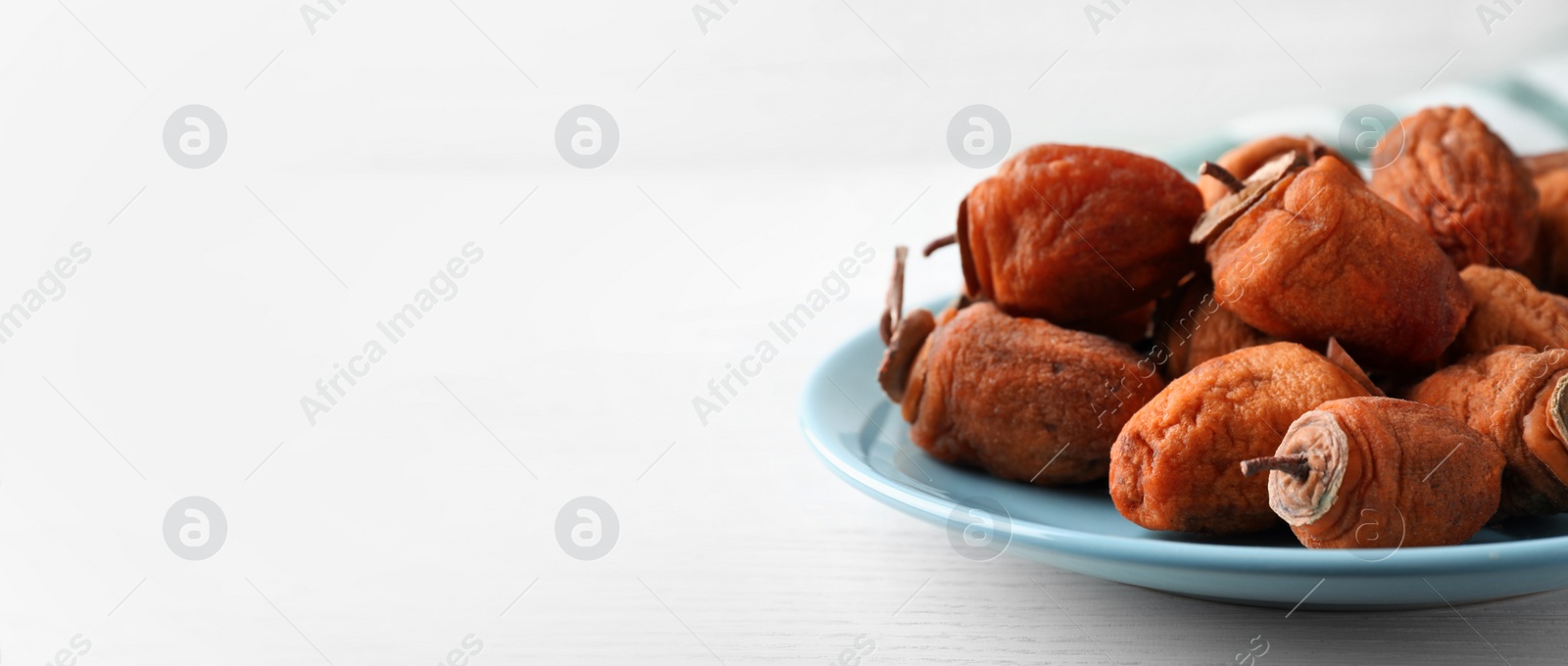 Image of Plate with tasty dried persimmon fruits on white wooden table, closeup view with space for text. Banner design