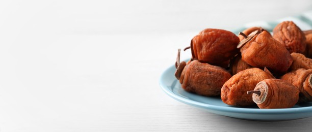 Plate with tasty dried persimmon fruits on white wooden table, closeup view with space for text. Banner design