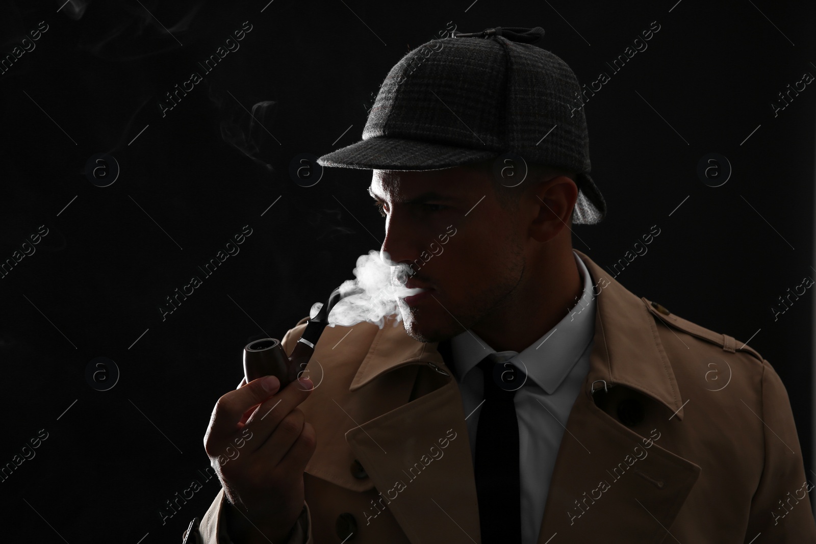 Photo of Old fashioned detective smoking pipe on dark background