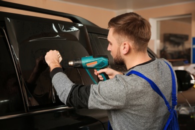 Photo of Worker tinting car window with heat gun in shop