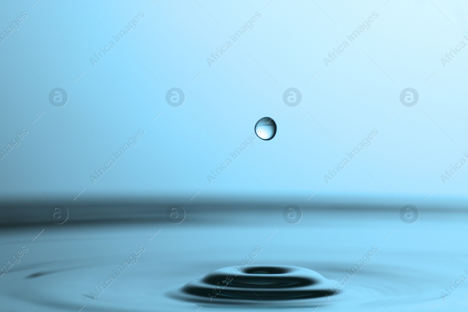 Photo of Drop falling into clear water on light grey background, closeup