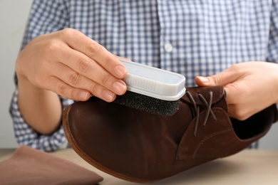 Photo of Woman taking care of stylish shoe at wooden table, closeup