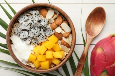 Photo of Bowl of granola with pitahaya, mango, almonds and yogurt on white wooden table, flat lay