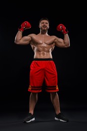 Photo of Man in boxing gloves celebrating victory on black background, low angle view