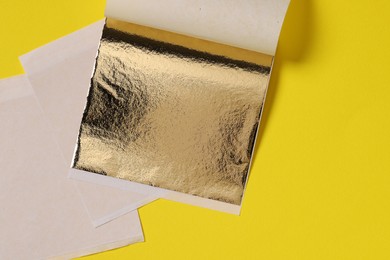 Photo of Edible gold leaf sheets on yellow background, top view