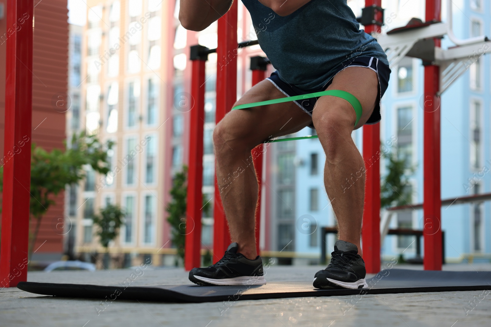 Photo of Muscular man doing exercise with elastic resistance band on mat at sports ground, closeup