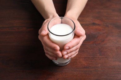 Photo of Woman holding glass of milk at wooden table, closeup