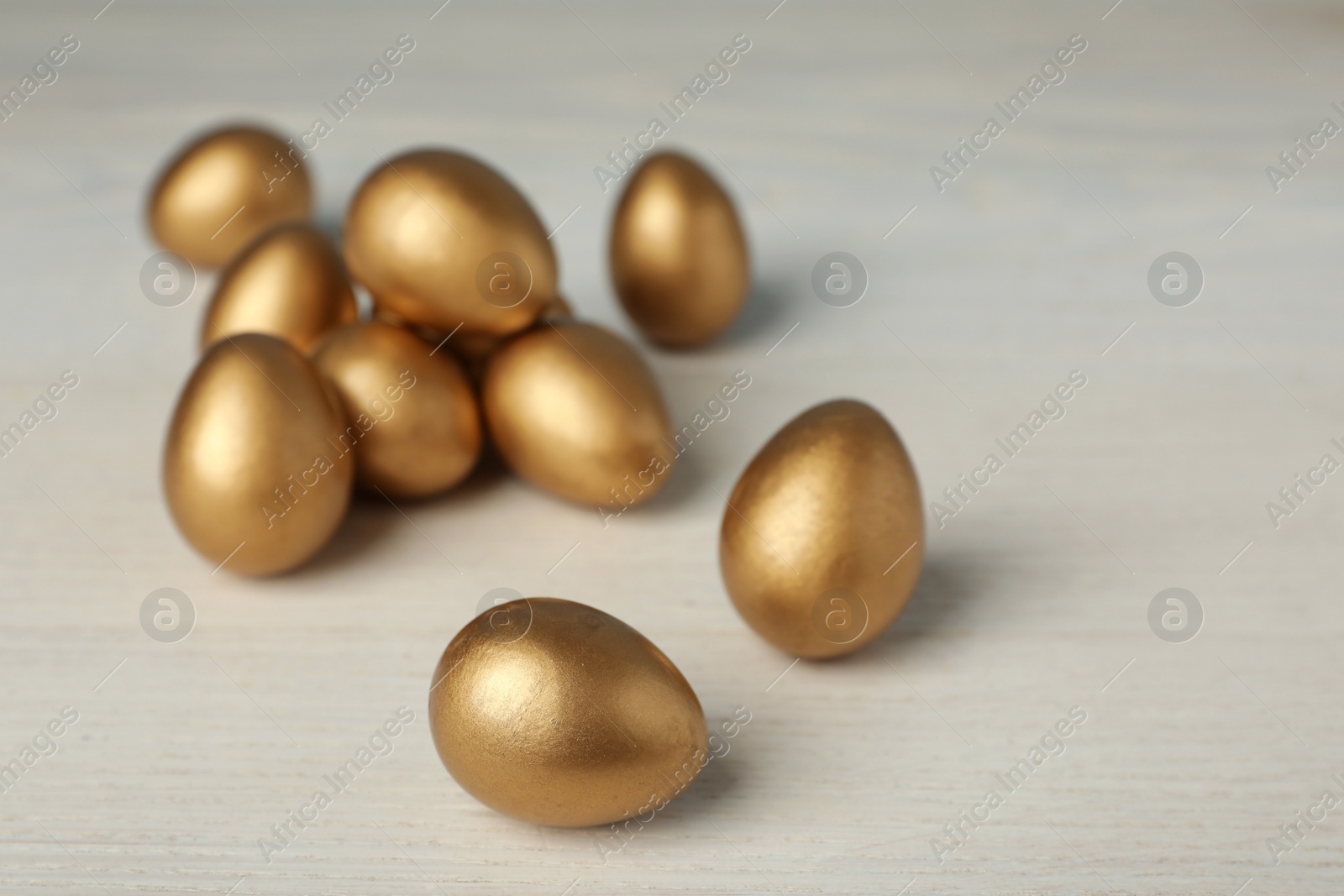 Photo of Shiny golden eggs on white wooden table