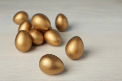 Shiny golden eggs on white wooden table