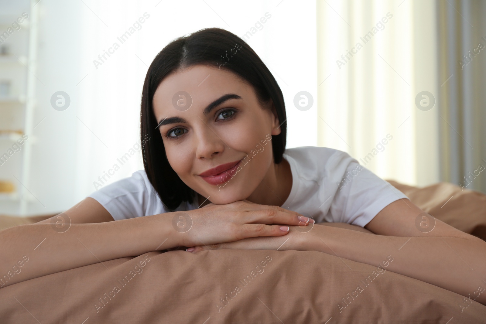 Photo of Young woman lying on bed with brown linens at home
