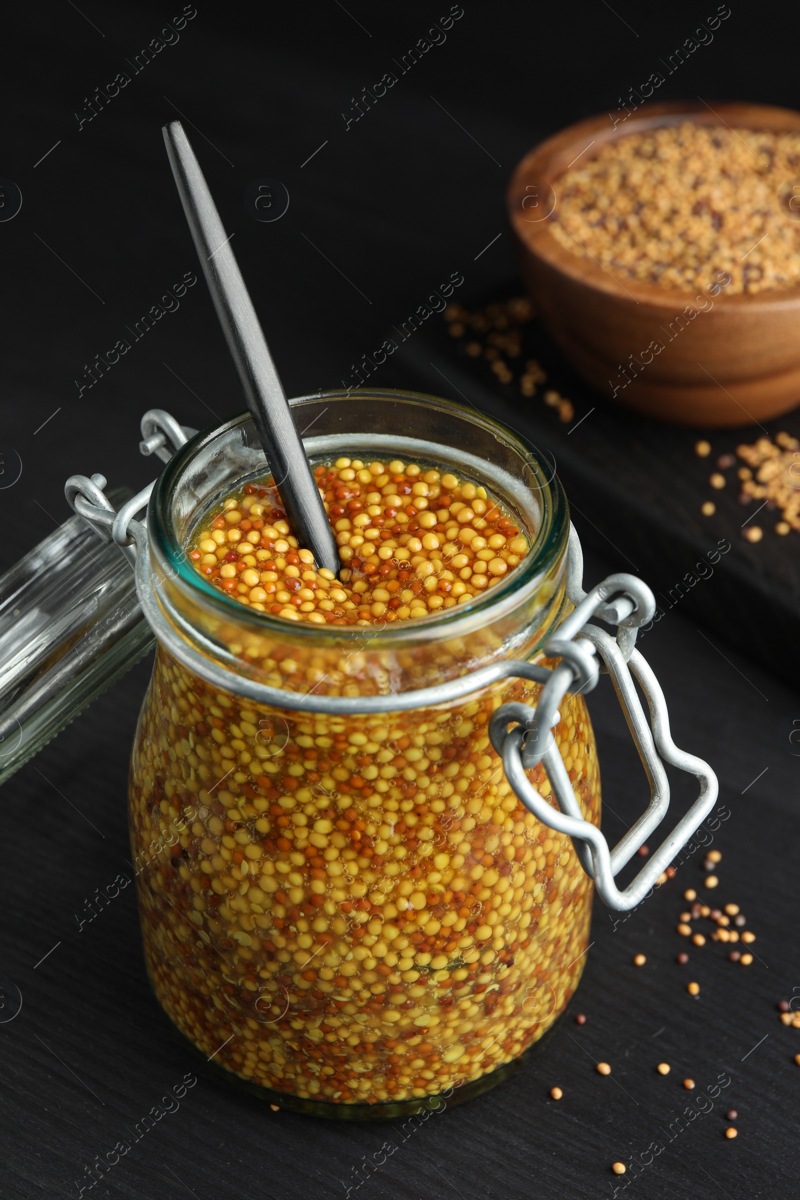 Photo of Whole grain mustard and spoon in jar on black wooden table