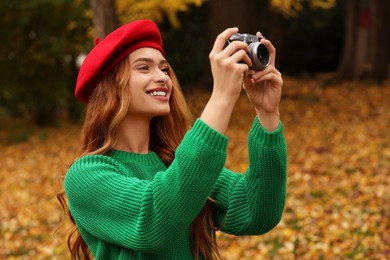 Photo of Smiling woman with camera taking photo in autumn park
