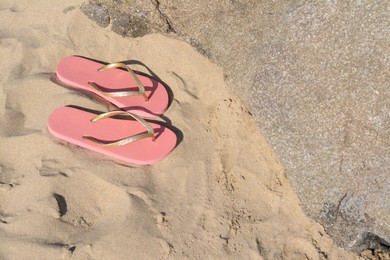 Photo of Stylish pink flip flops on sandy beach near rock