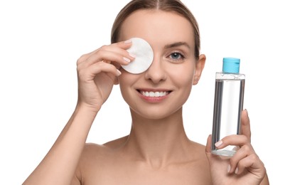 Photo of Smiling woman removing makeup with cotton pad and holding bottle on white background